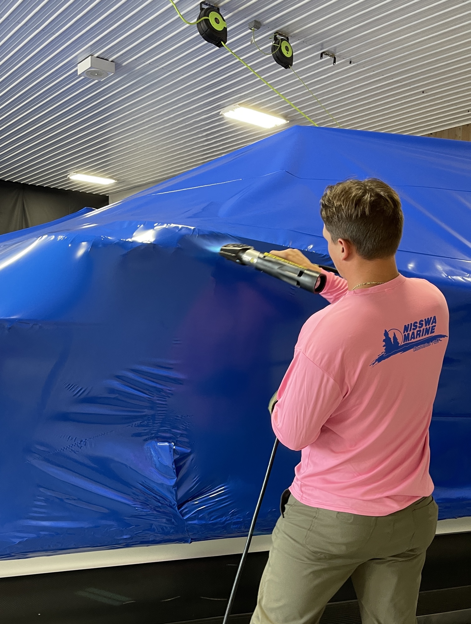 A man applying heat to a cover so it conforms to a boat's structure in the shop
