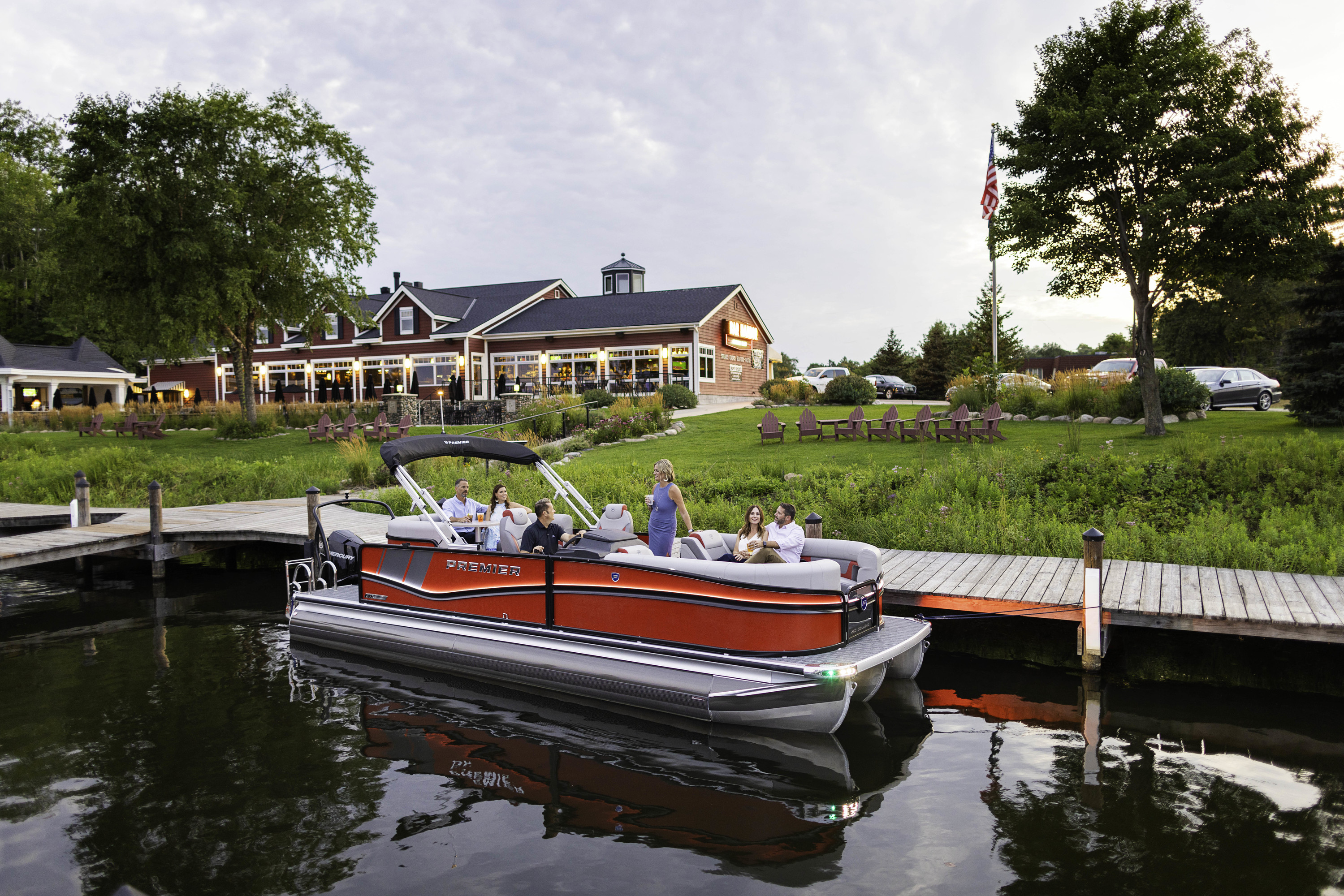A Premier® SunStation pontoon boat that's docked on land while several people play volley a ball …
